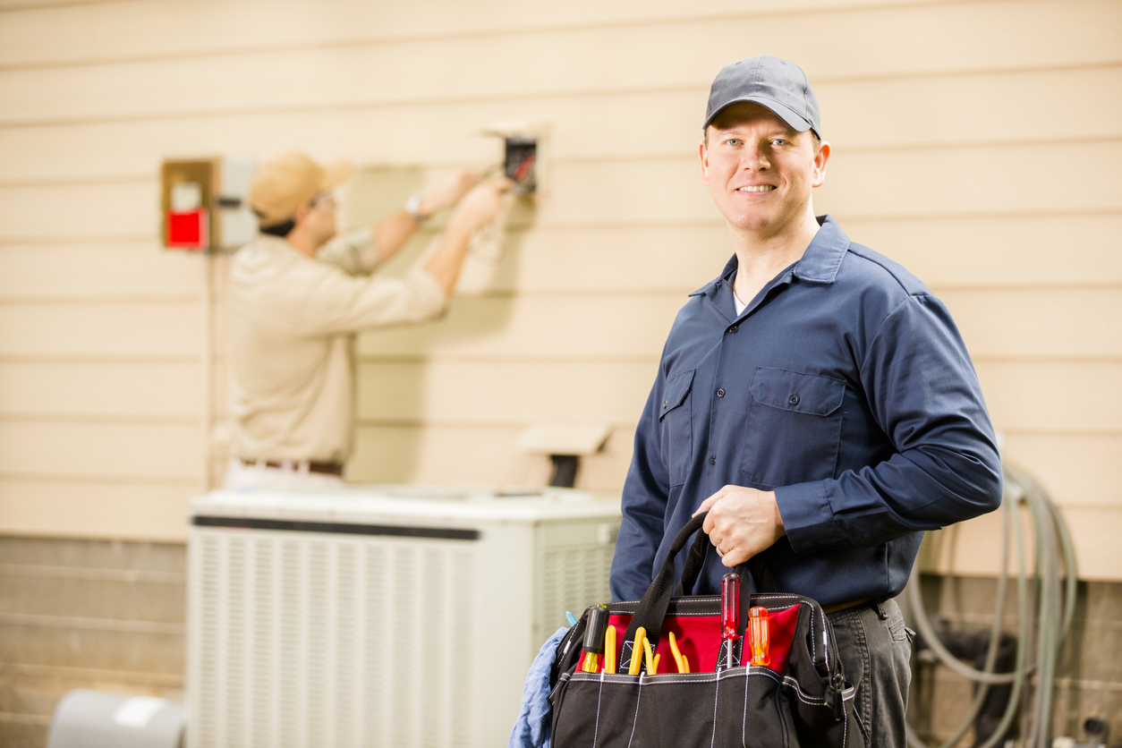 Air conditioner repairmen work on home unit. Blue collar workers.